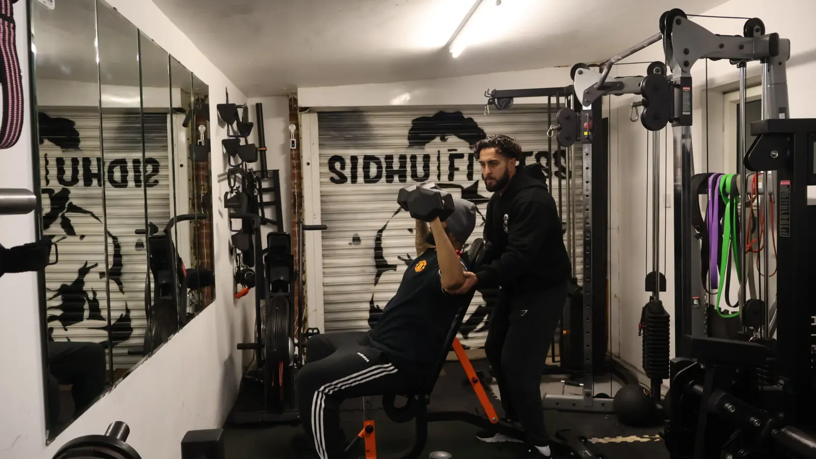 Tony Sidhu closely coaching a male client through an incline dumbbell press in the private studio