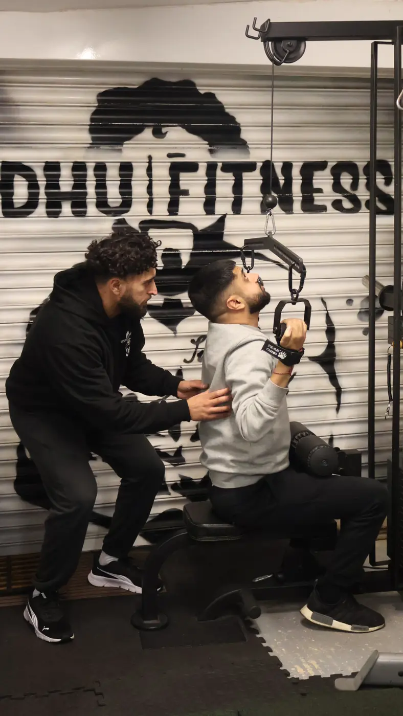 Tony Sidhu correcting a male client's torso position during a close-grip lat pulldown in the private studio