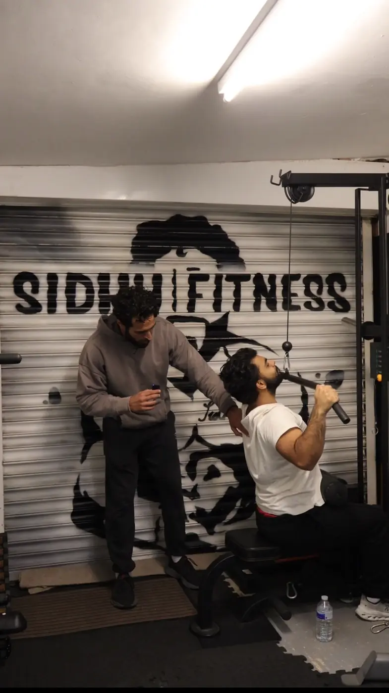 Tony Sidhu observing and coaching a male client performing a lat pulldown at Sidhu Fitness
