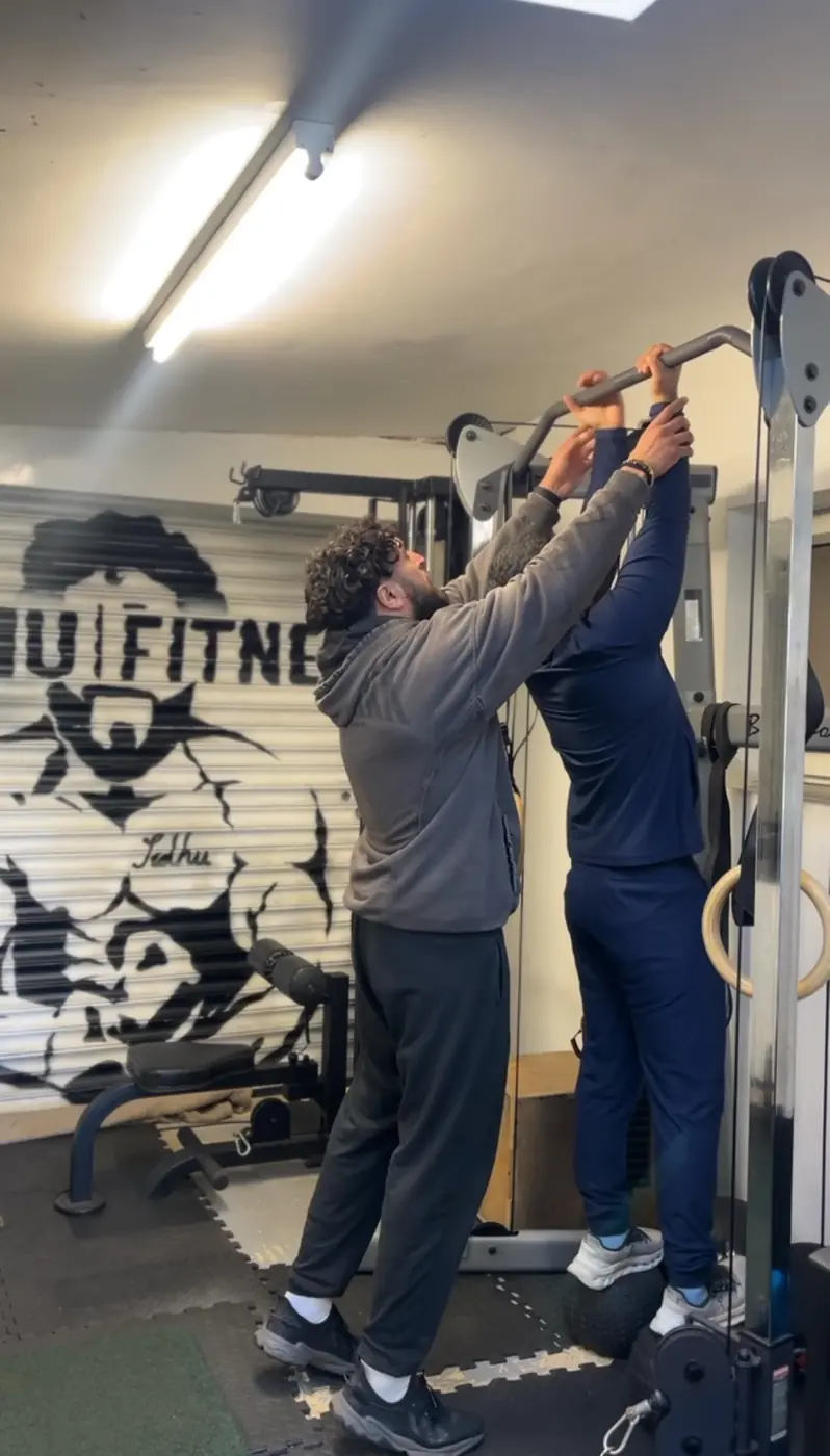 Tony Sidhu assisting a client with upper-body positioning during a coached cable exercise