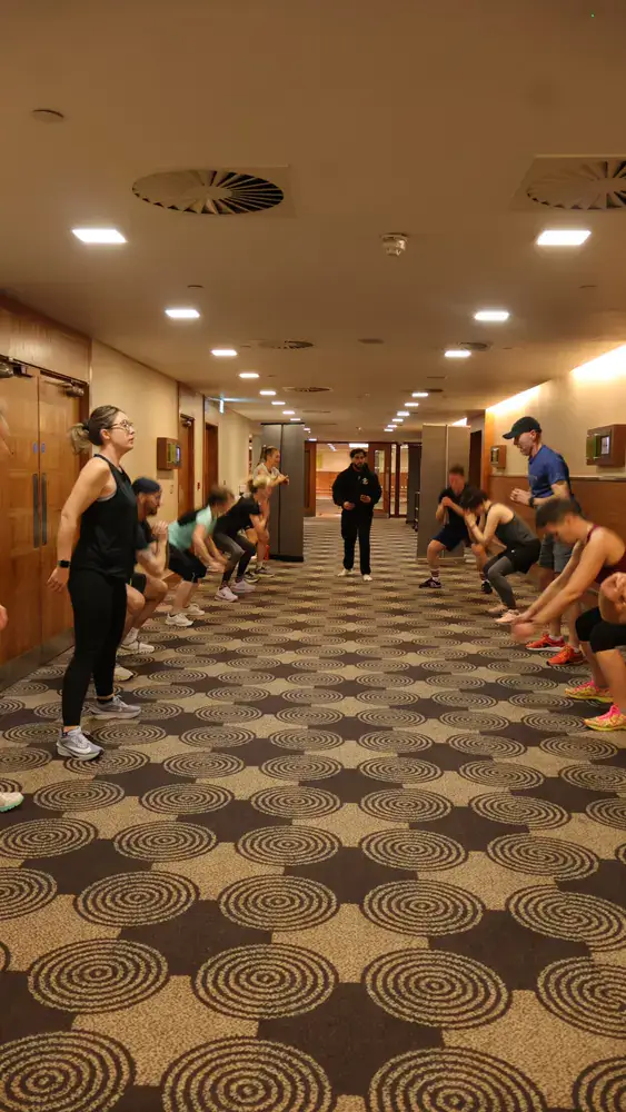 Workplace wellbeing group completing a coached squat exercise during a Sidhu Fitness team session
